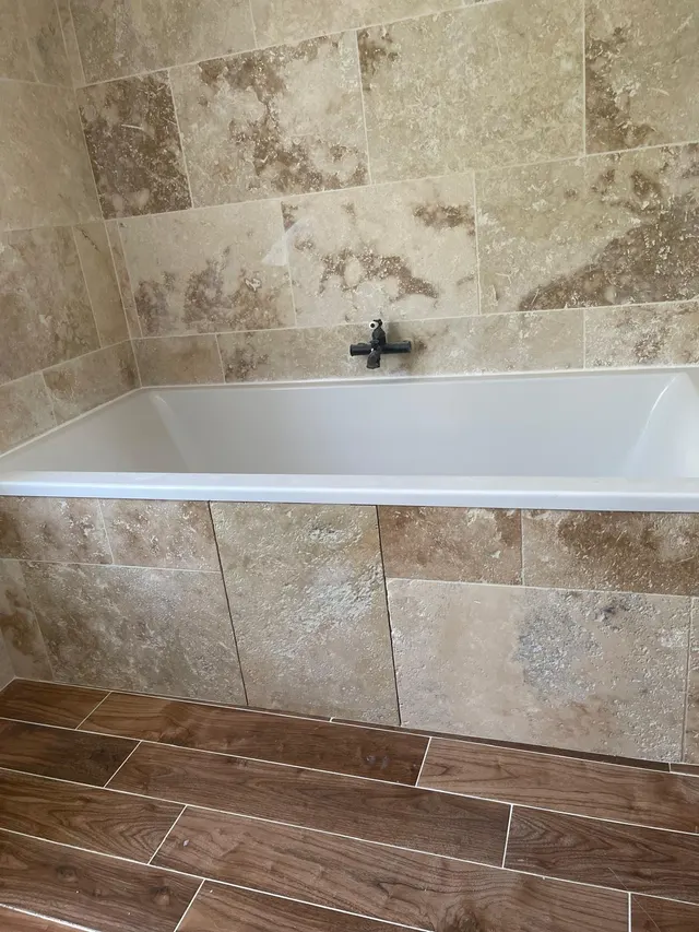 Baignoire encastrée, tablier et murs en travertin, sol en carrelage imitation bois foncé