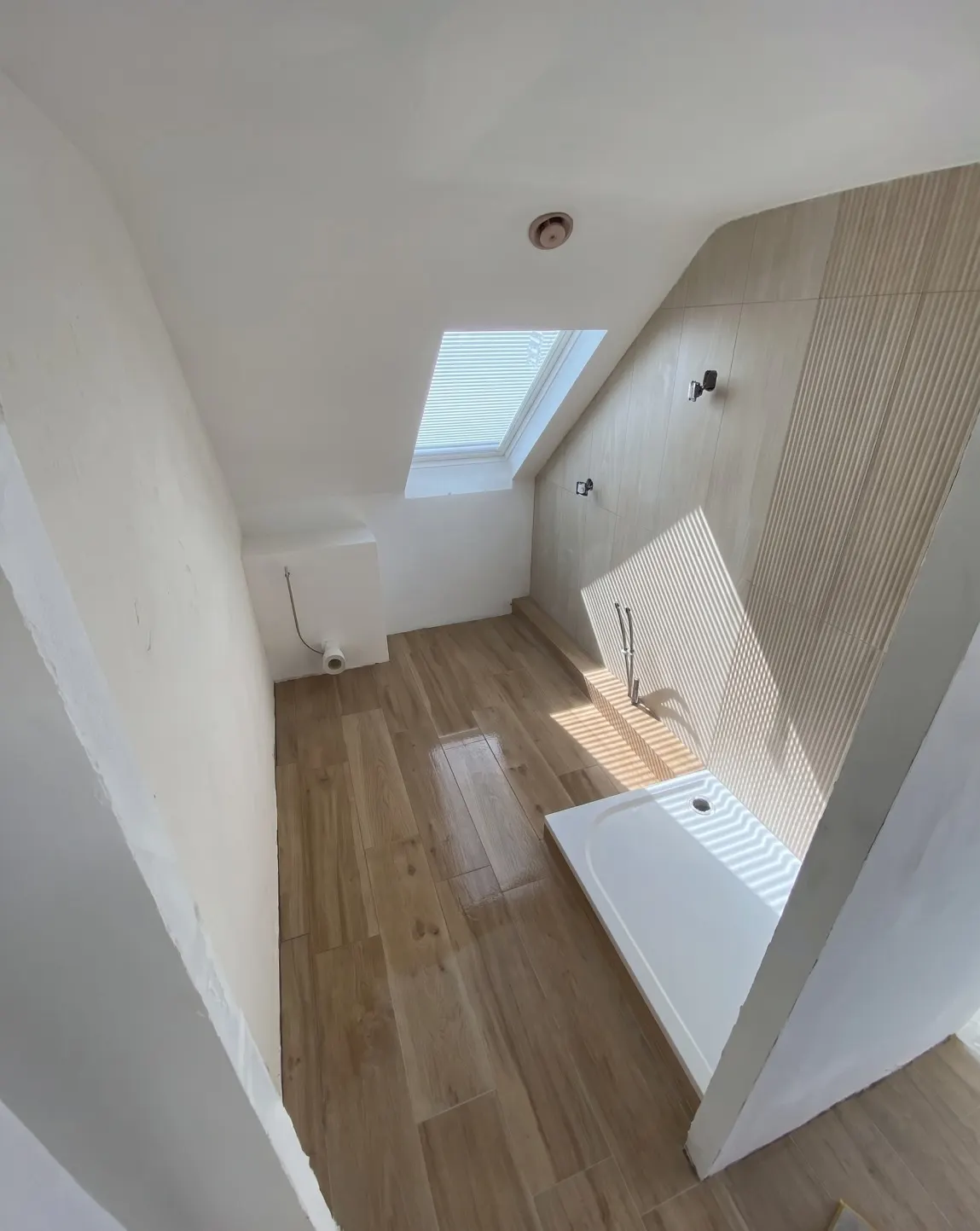 Salle de bains sous combles : sol imitation parquet, mur de faïence effet bois striée, receveur blanc