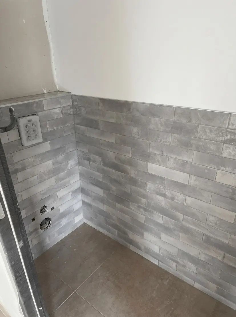Mur de faïence grise façon brique à mi-hauteur, sol en grands carreaux