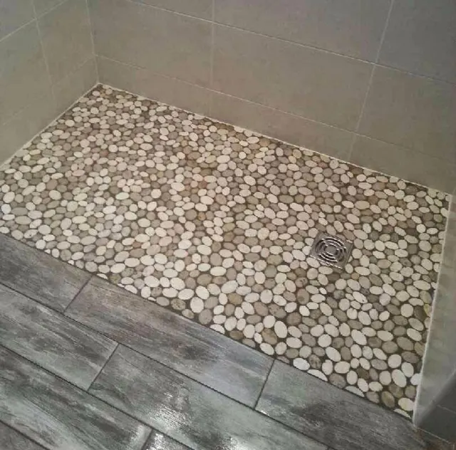 Sol de douche en mosaïque de galets, bordé d'un carrelage imitation bois gris