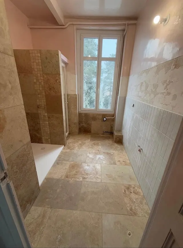 Salle de bains au sol en travertin, douche habillée de mosaïque, faïence beige au mur