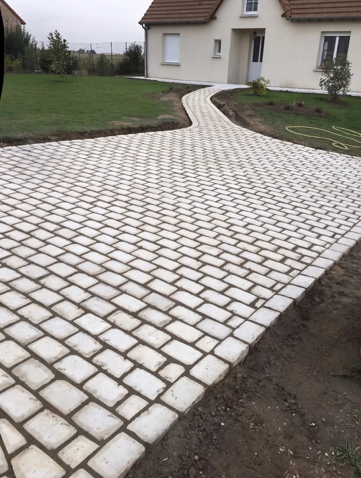Allée en pavés clairs qui serpente jusqu'à une maison, entre deux pelouses